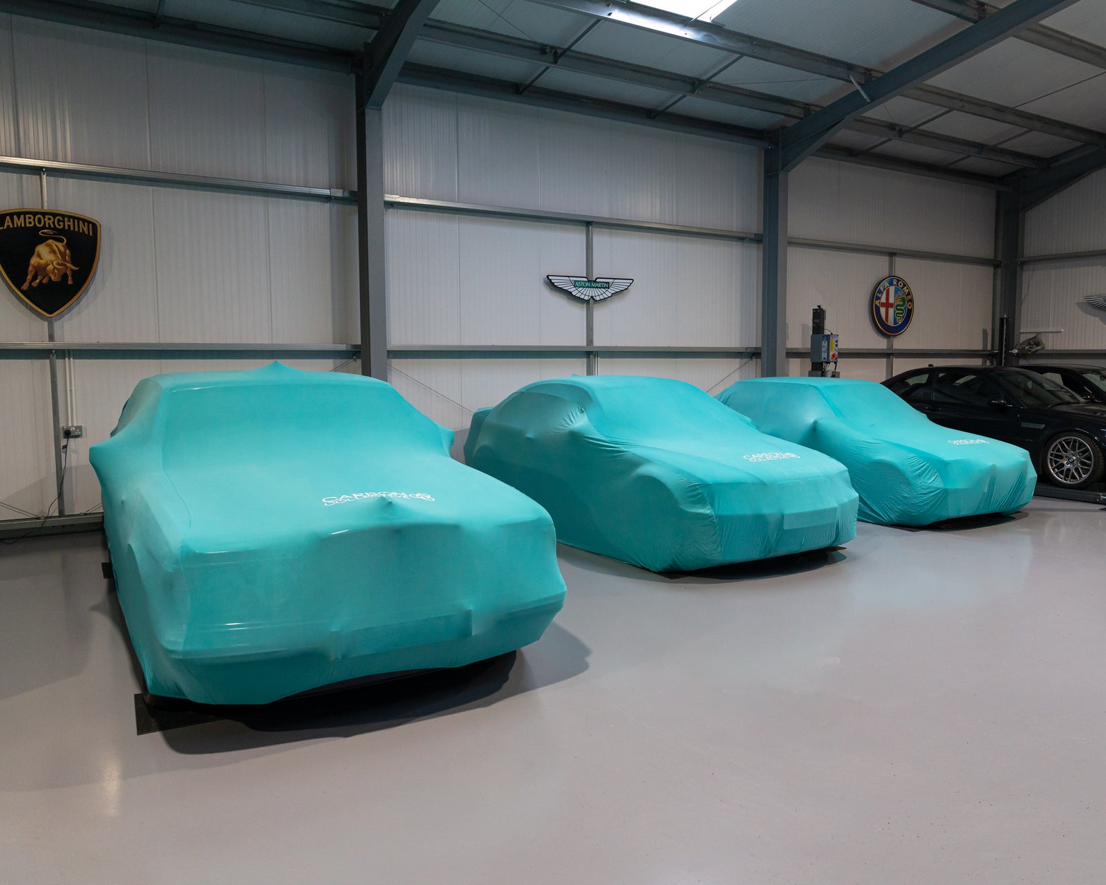 Three teal blue carbon collective indoor car covers fitted on vehicles inside a storage facility