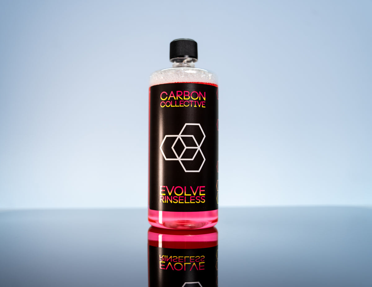 A bottle of Carbon Collective EVOLVE Rinseless Cleaner on a reflective surface.
